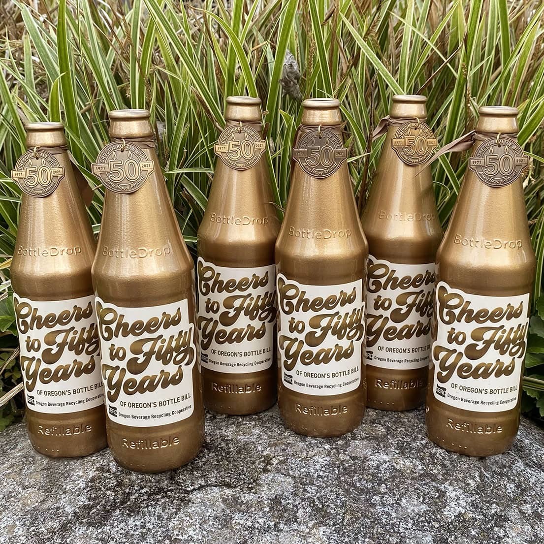 Five golden bottles for the OBRC 50th anniversary treasure hunt, photographed outdoors on a rock.