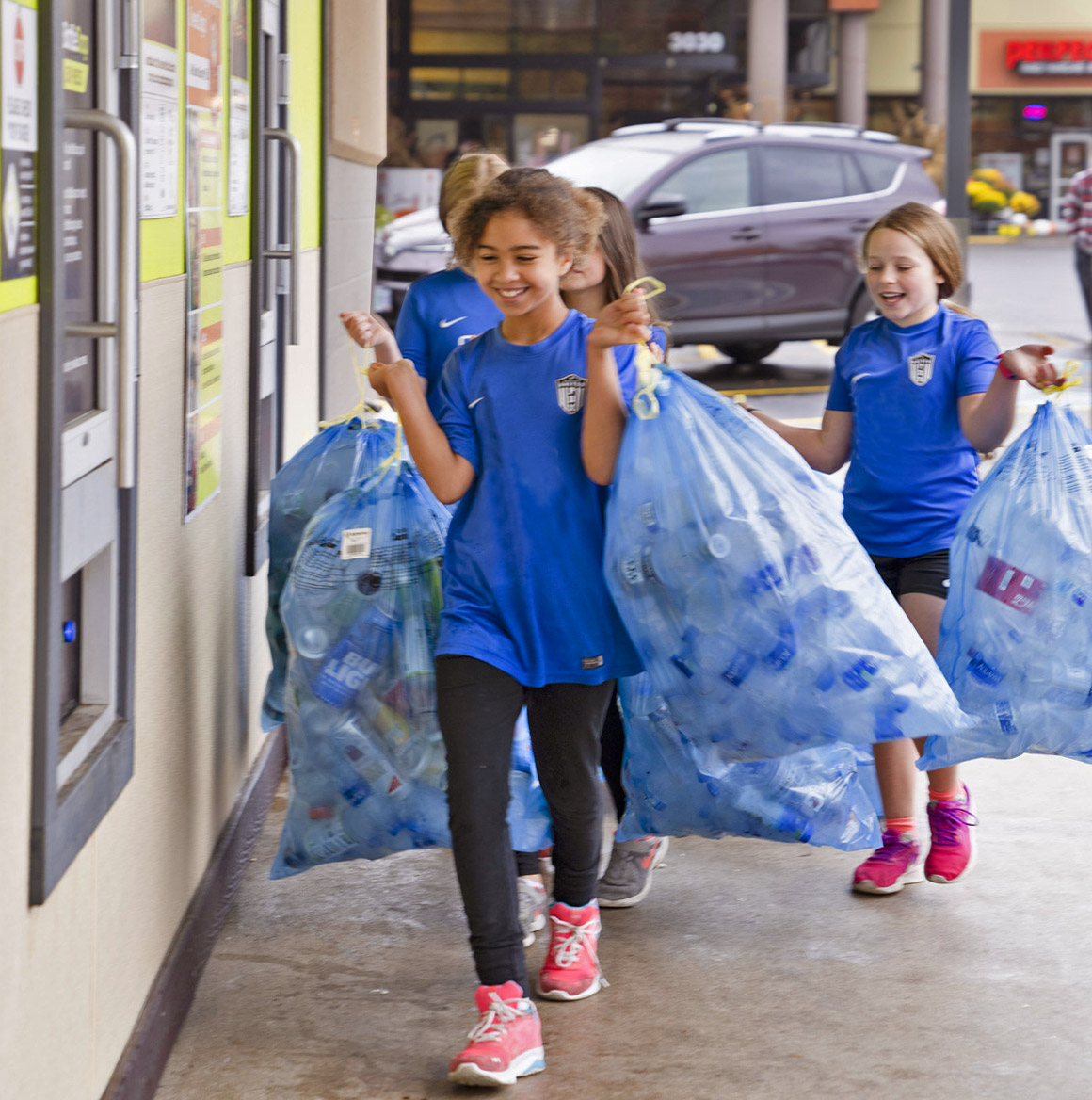 Three happy kids carrying blue bags full of recyclable containers to OBRC's Containers for Change program.