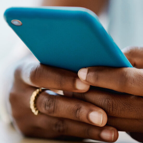 Close up of the hands of a young Black woman checking her cellphone.