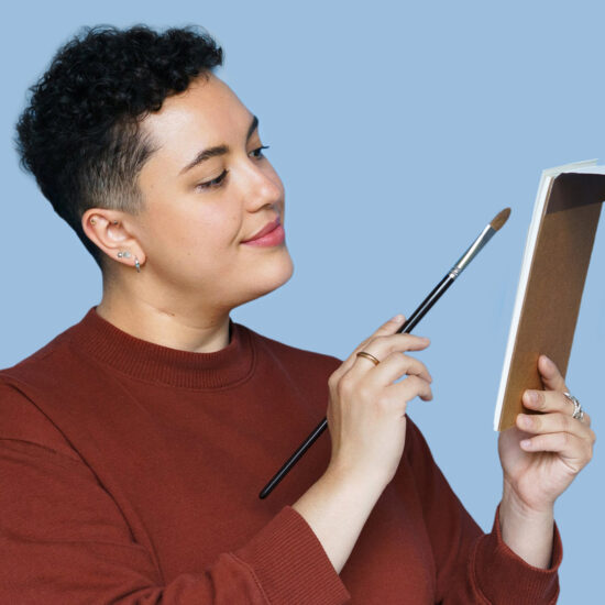 Liz Vargas holding a paintbrush and notebook.