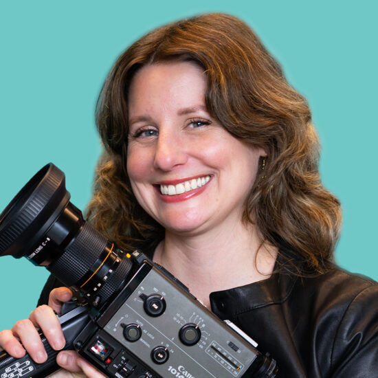 A smiling woman with shoulder-length brown hair holding a video camera.