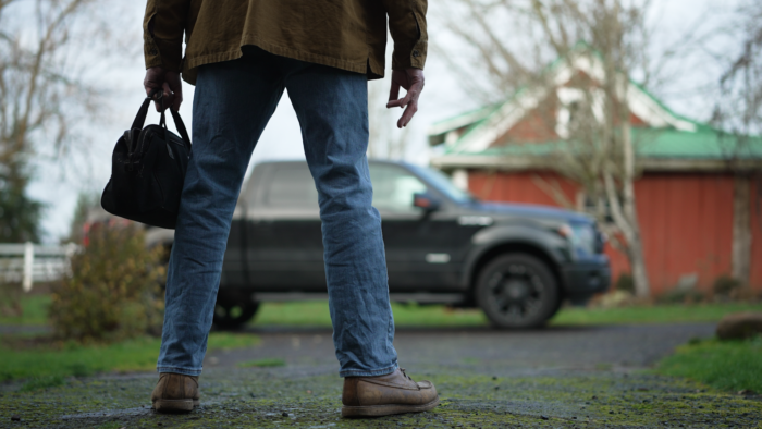 A man stands near a pickup truck in a showdown kind of pose. 