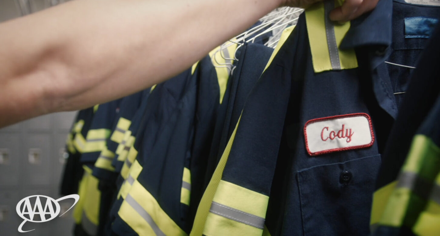 Still from the "More than a Job" video from AAA, showing an employee getting ready to put on his uniform jacket with his embroidered name "Cody".