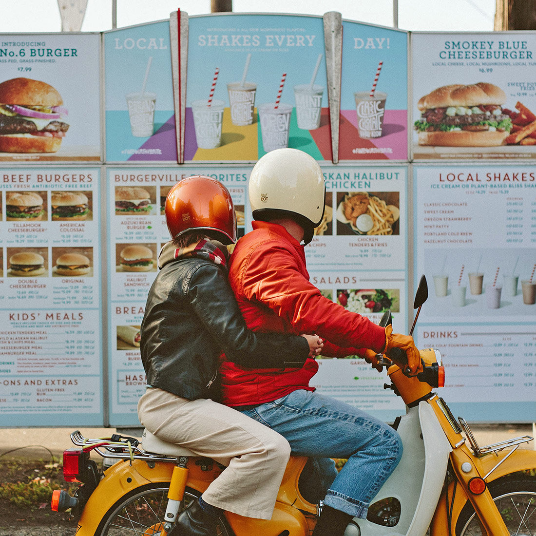 Two Burgerville patrons on a vintage moped peruse the drive-through menu board.