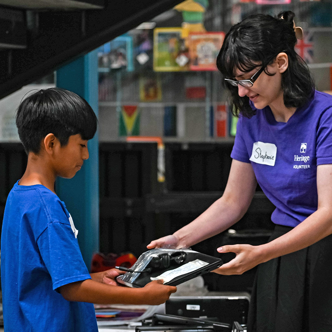 A volunteer hands a tablet device to a young boy.