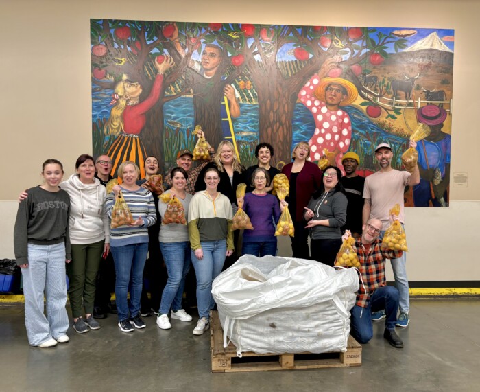 A group of people standing in front of a colorful mural holding bags of potatoes.