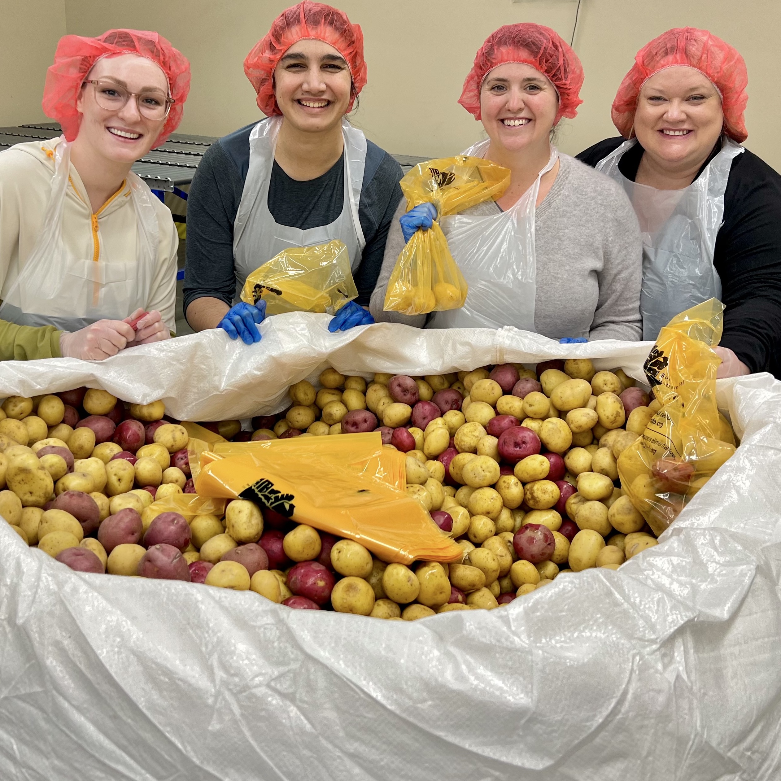 Four women in red hair nets putting potatoes in a bag.
