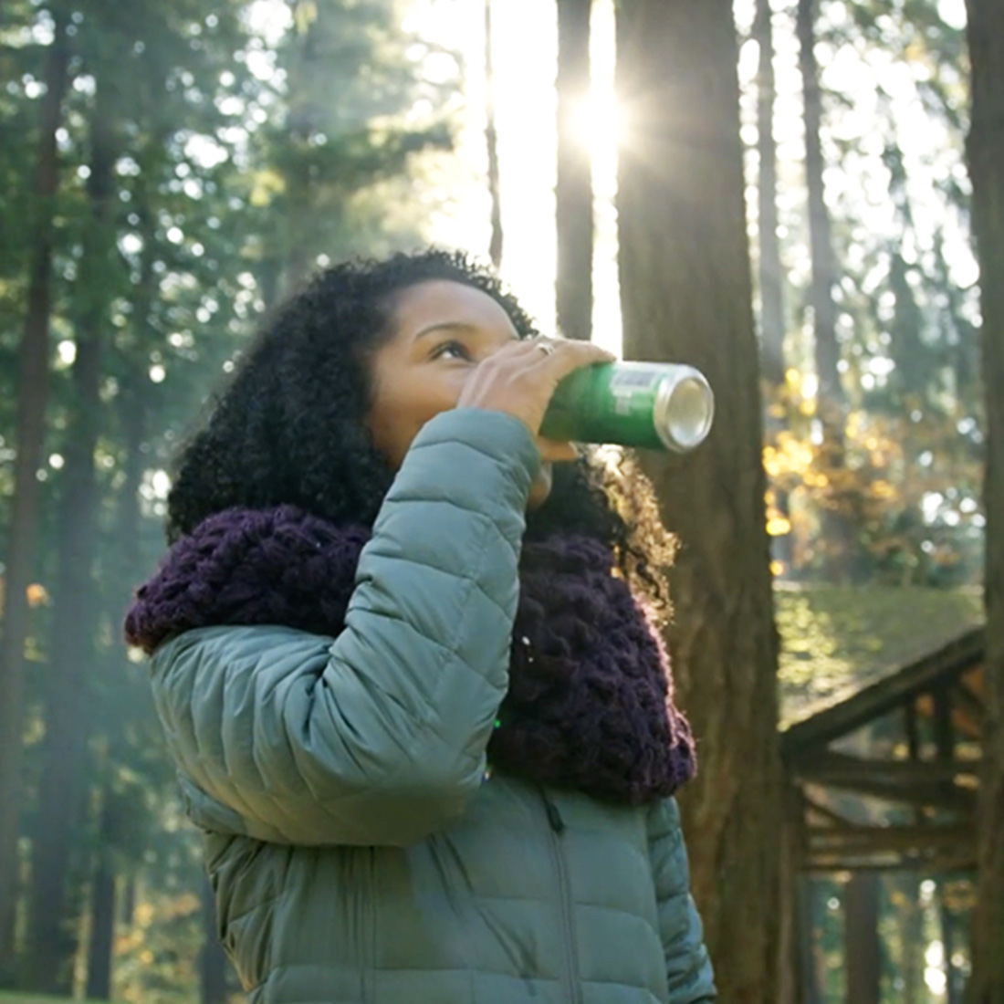 A screenshot from Oregon Beverage Recycling Cooperative's Green Bags video of a woman in a forest drinking a canned beverage.