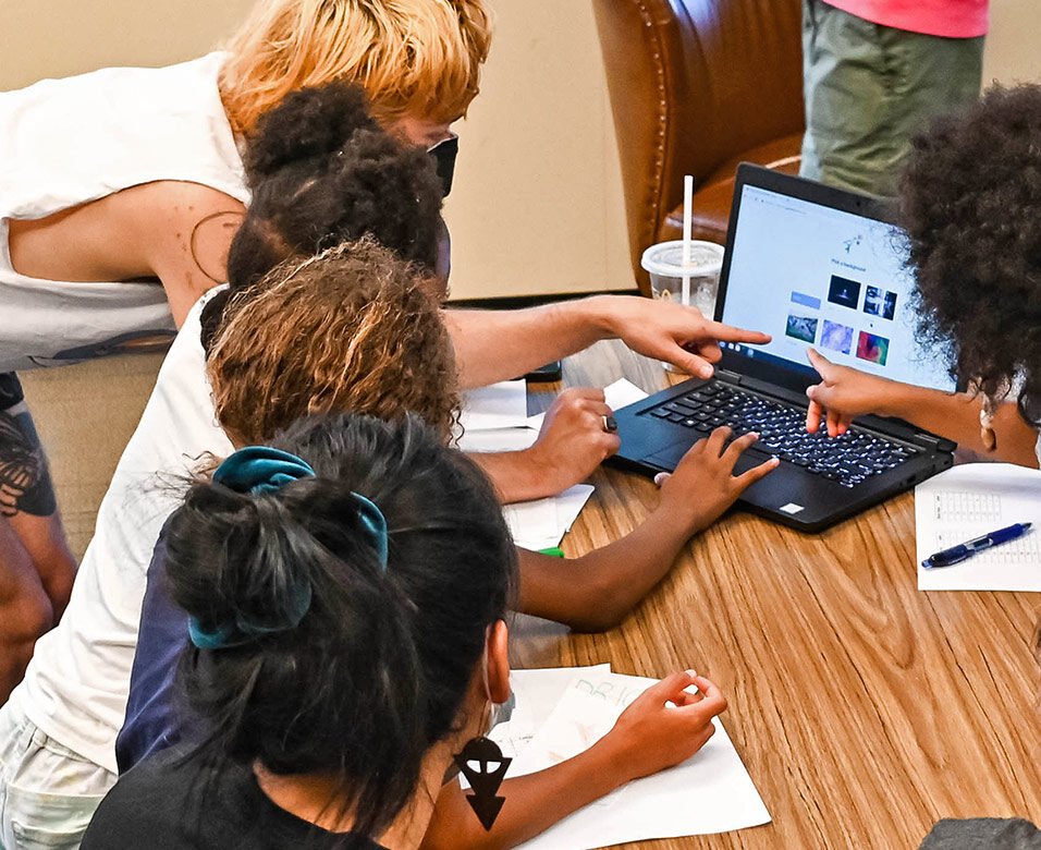 Kids gather around a laptop on a table.