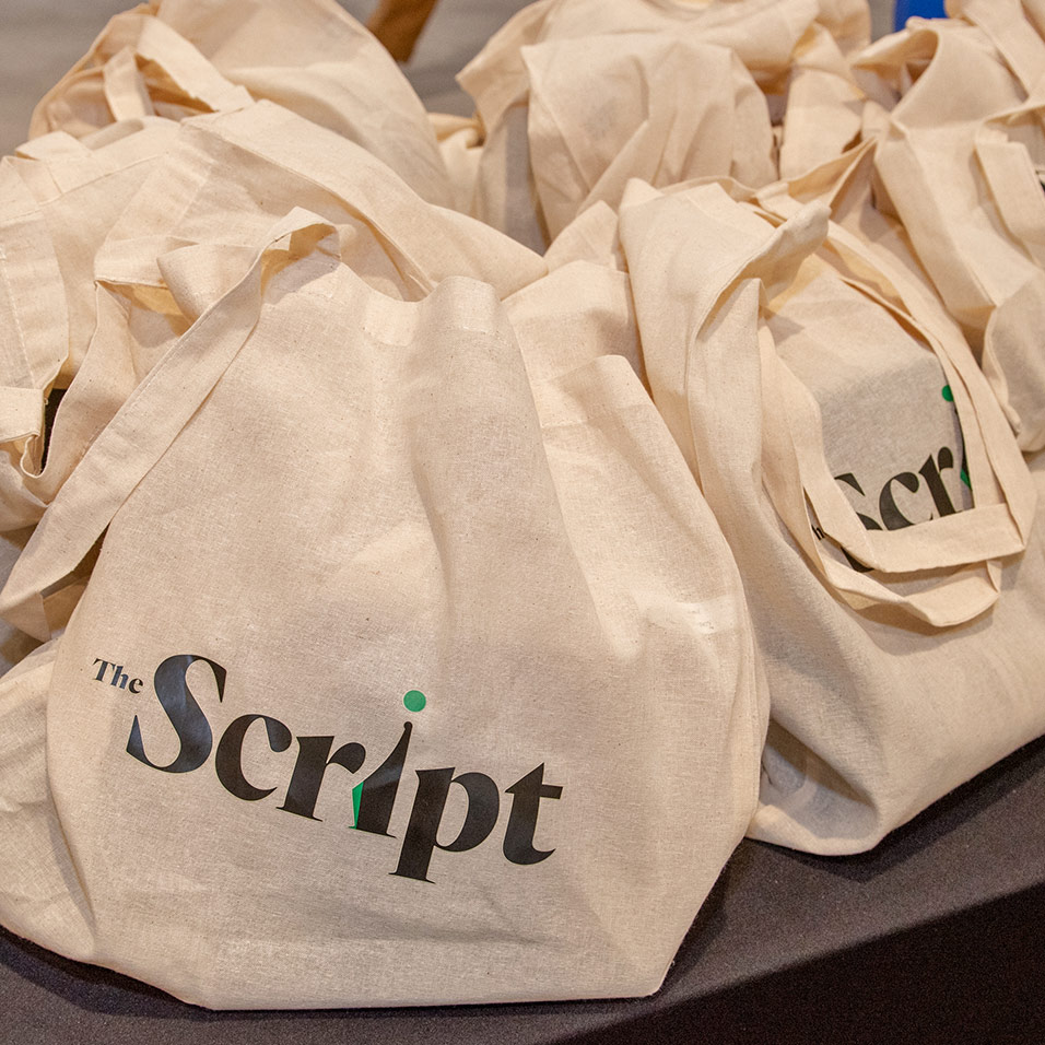 A pile of tote bags with The Script logo.