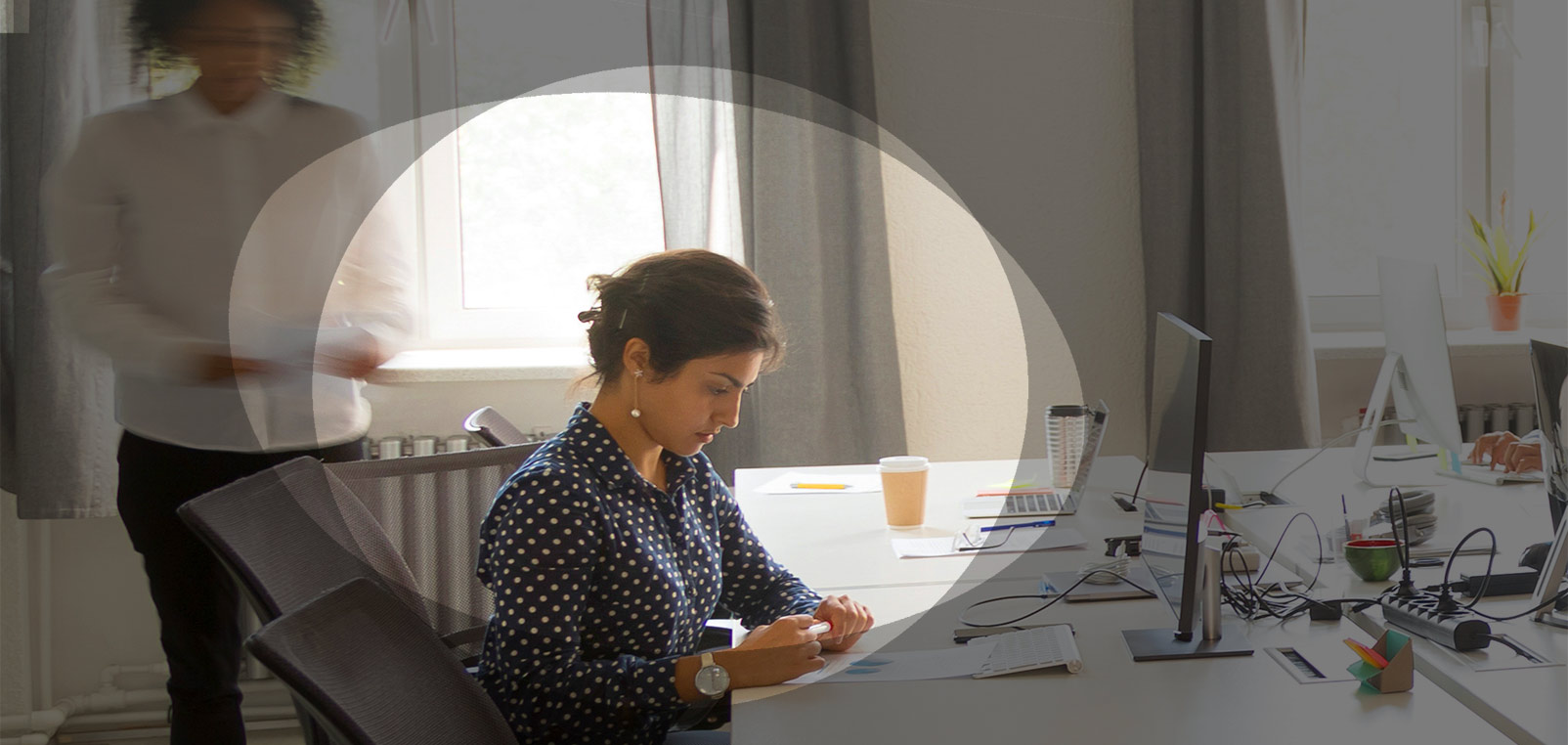 A young woman at a desk in an office reads a course syllabus in preparation for an online training course.