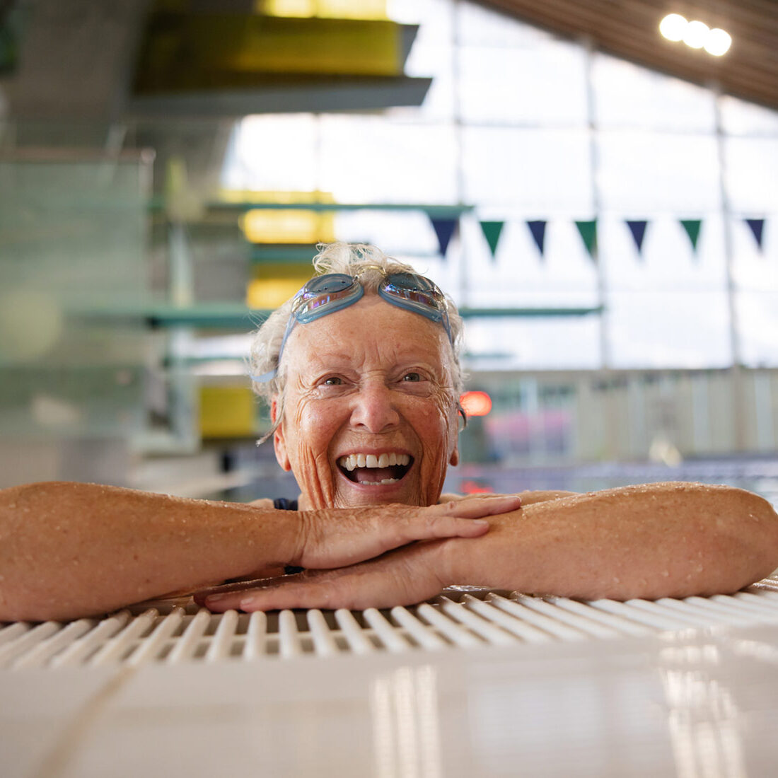 A woman in her 70s laughs as she emerges from doing laps in an indoor pool.