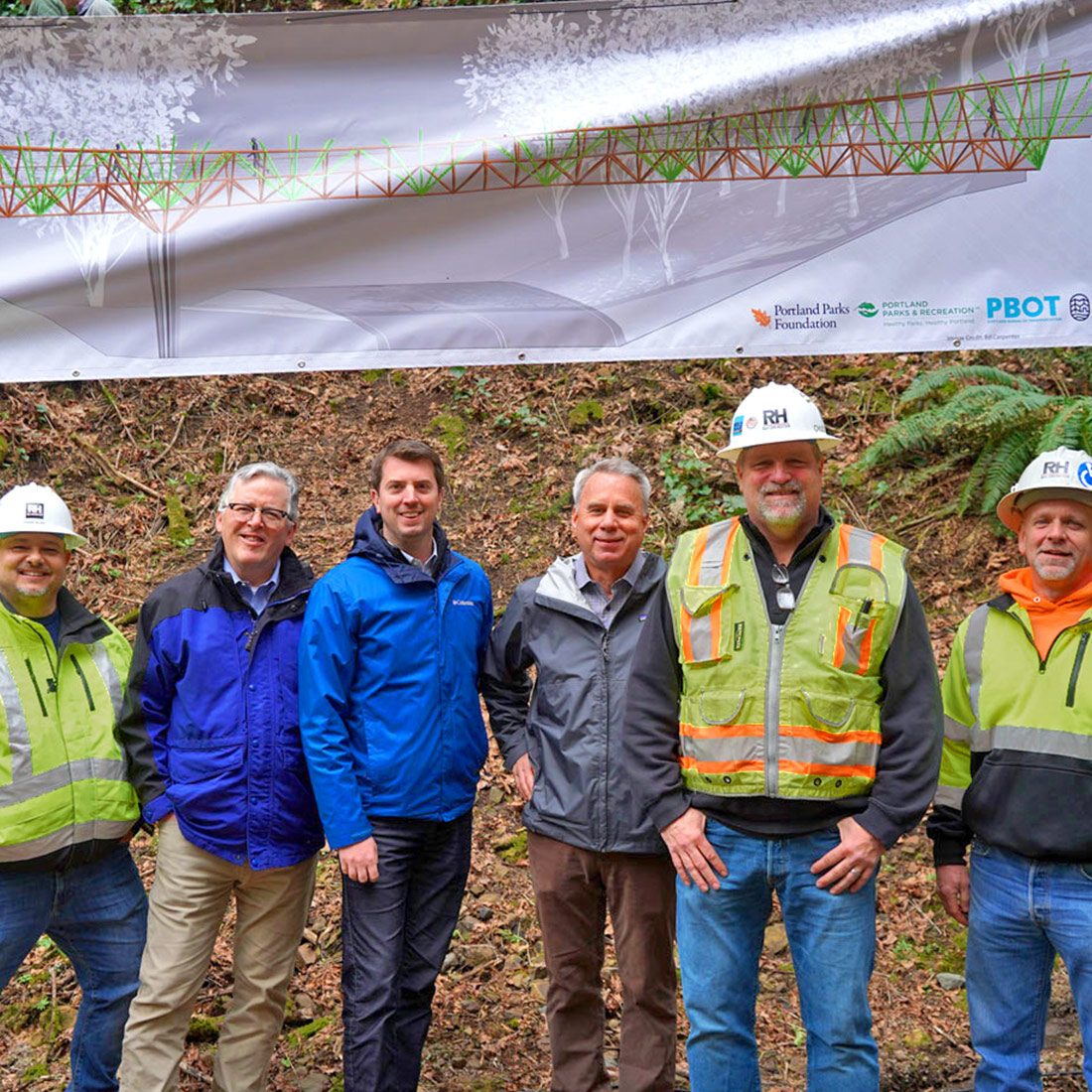 Workers pose beneath a banner during the Barbara Walker Crossing Groundbreaking event.