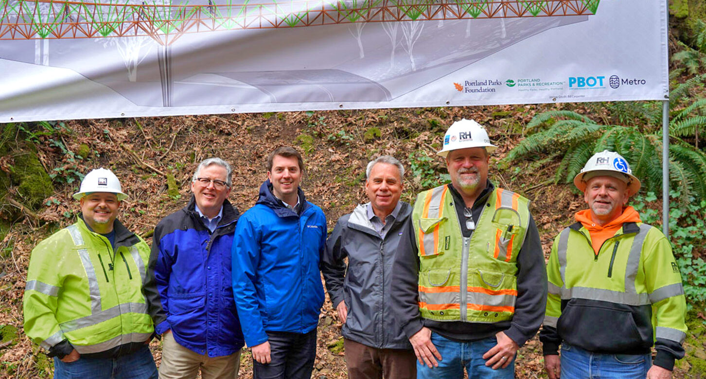 Workers pose beneath a banner during the Barbara Walker Crossing Groundbreaking event.