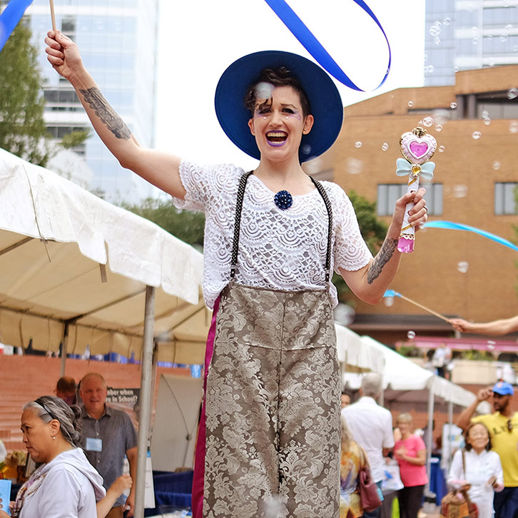 A laughing stilt-walker parades while swirling a blue ribbon during The Standard's annual volunteer expo in Portland, Oregon.