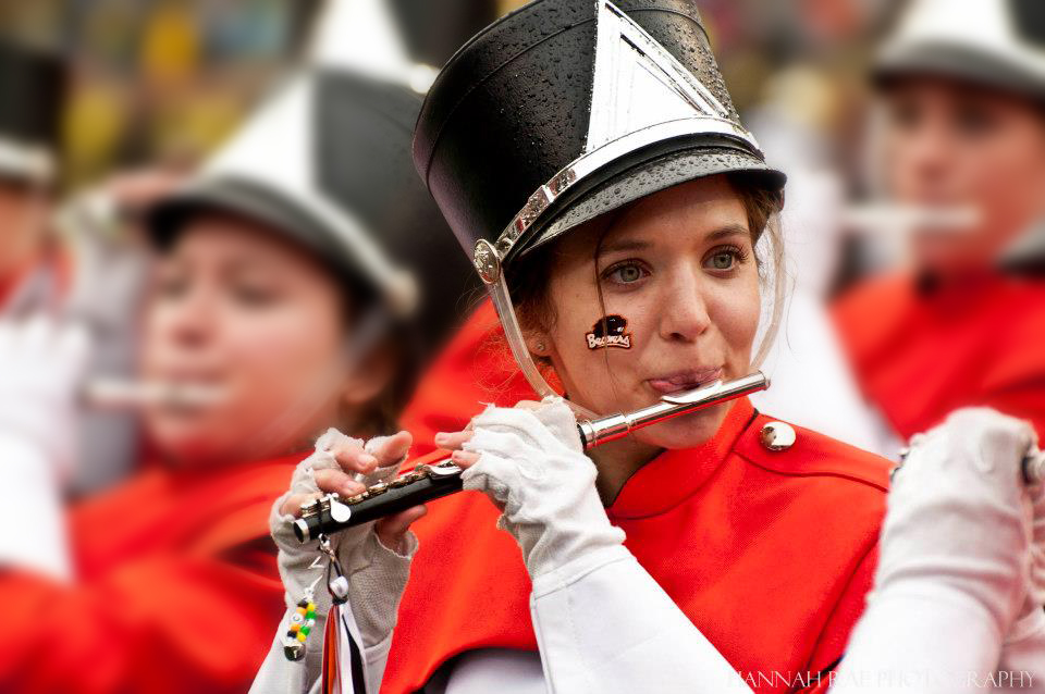 A young woman in a black and red marching band uniform playing piccolo in a band.