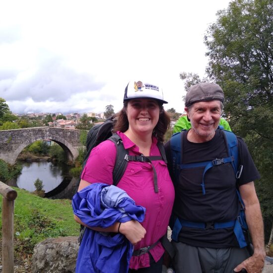 A woman and a man backpacking near a river and a stone bridge in Spain.