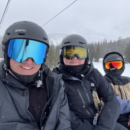 Three skiers in helmets and goggles on a ski lift.