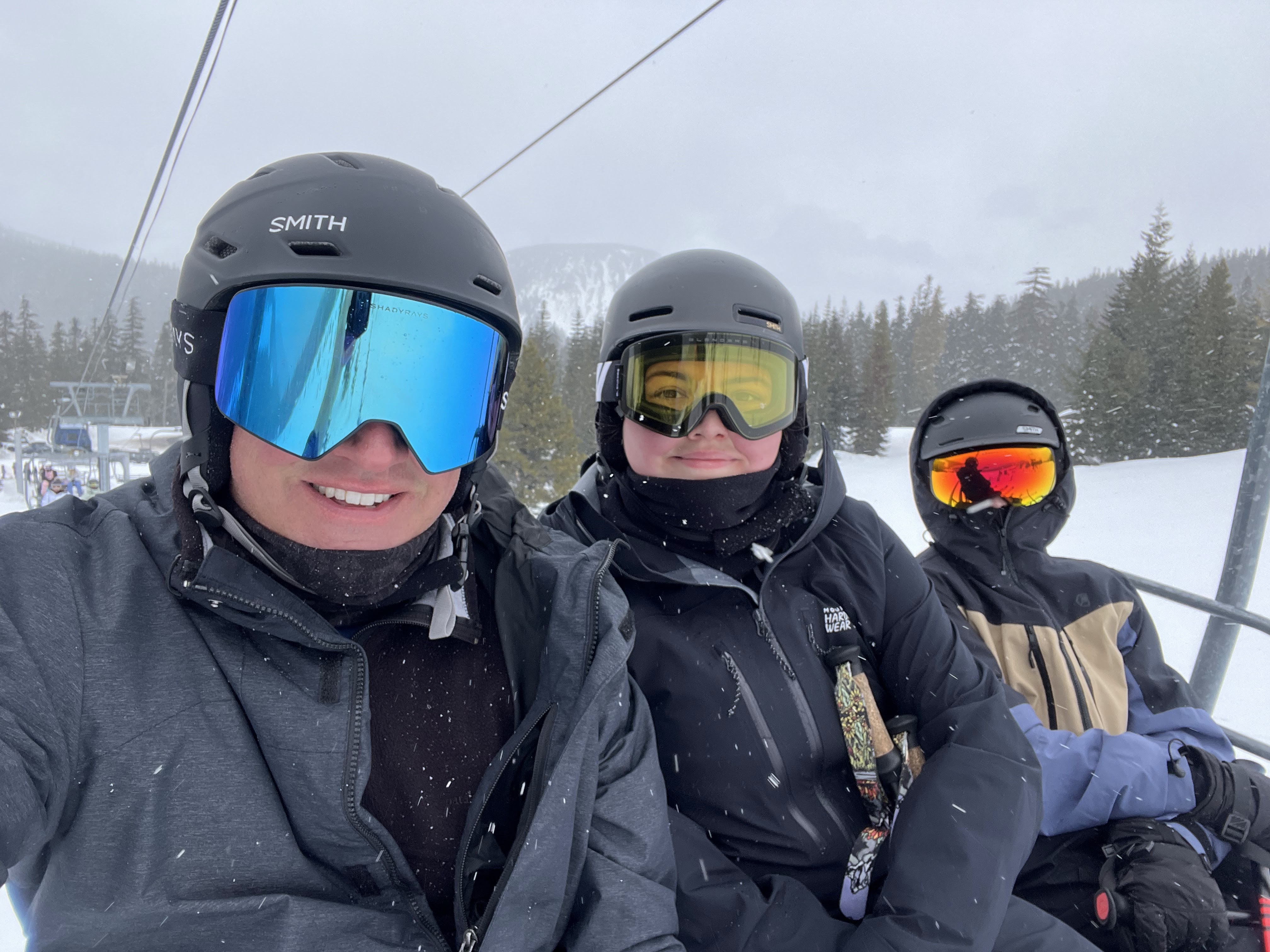 Three skiers in helmets and goggles on a ski lift.