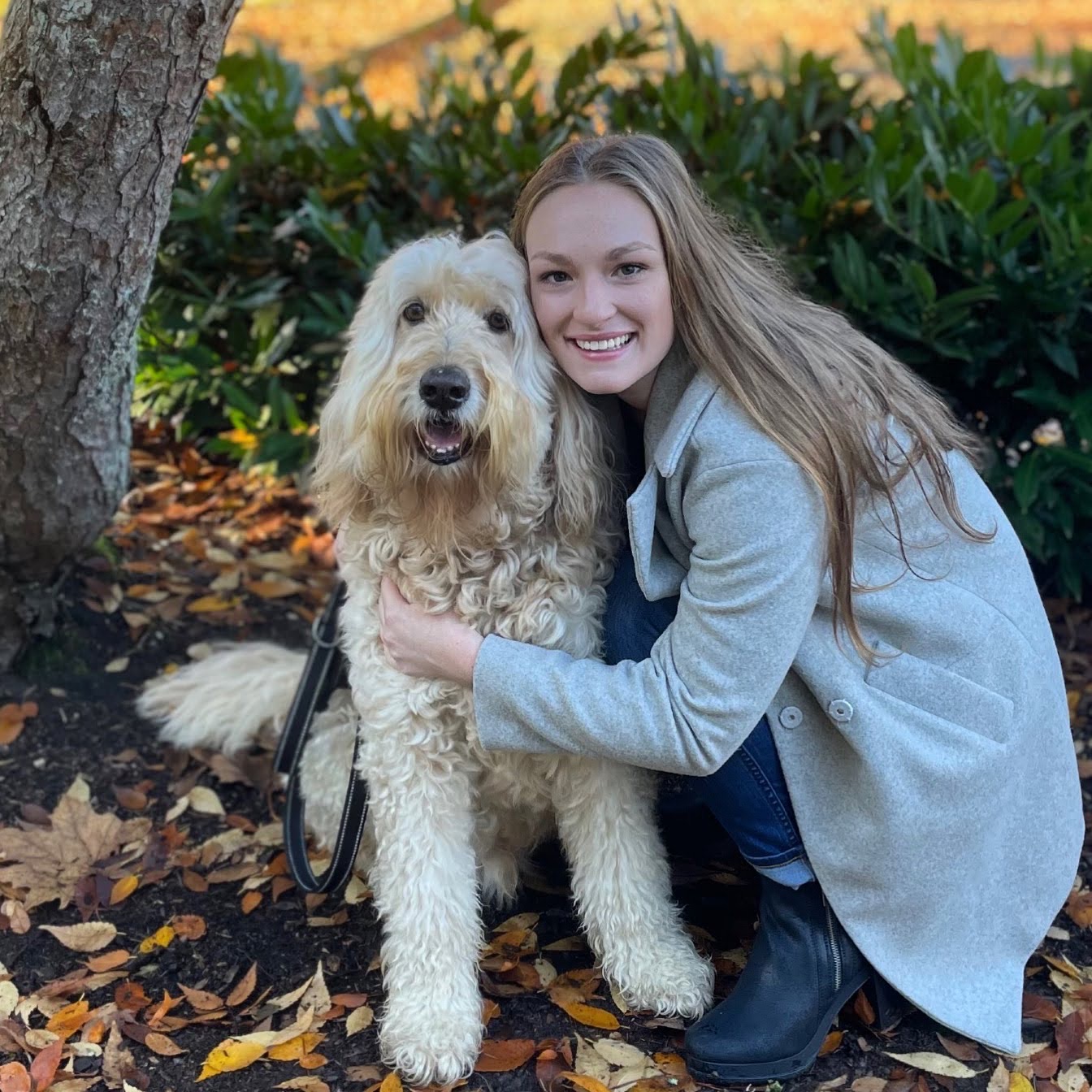 A woman hugging her dog outside by a tree.