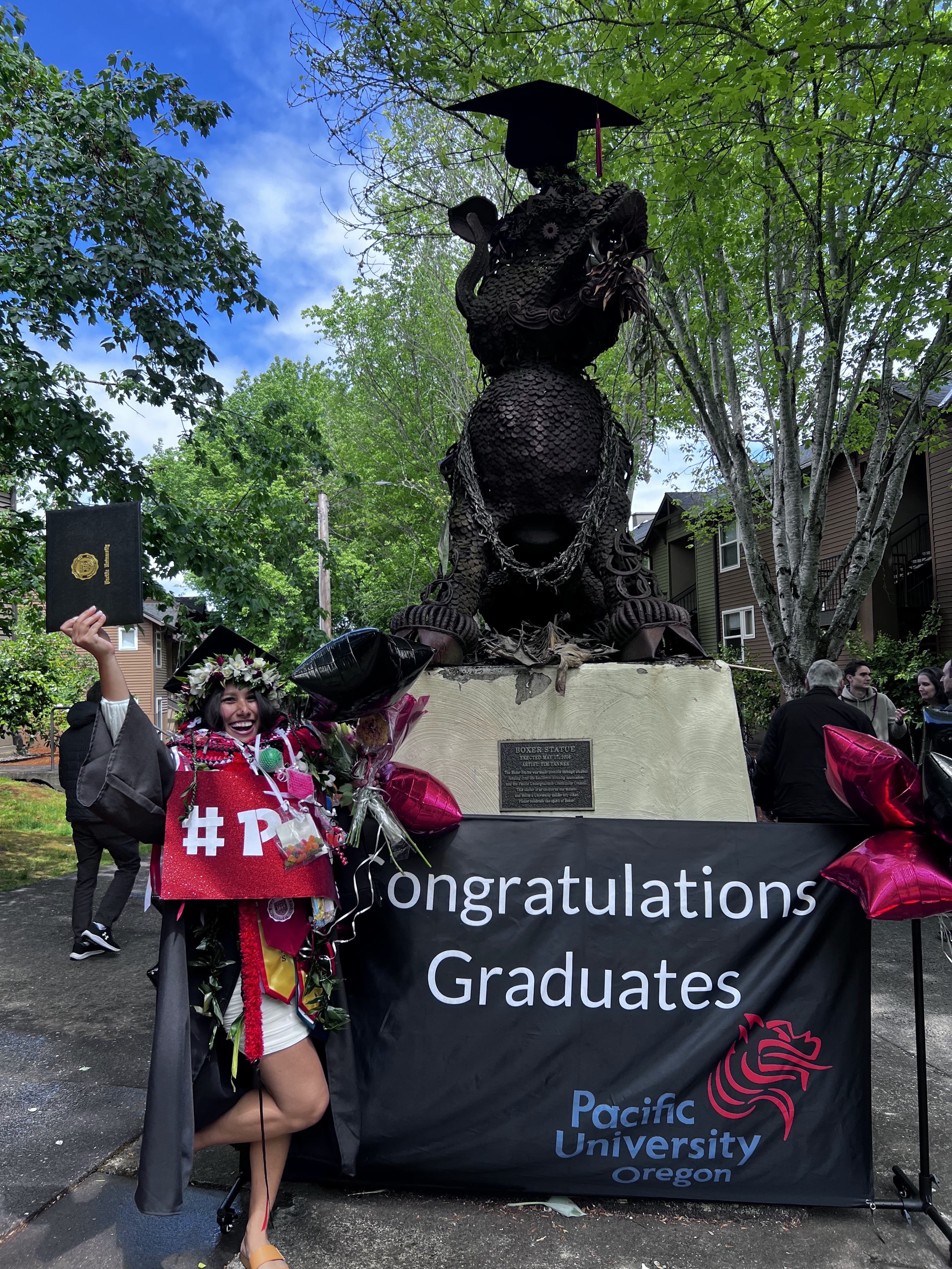 Mahia LaBoy in her cap and gown celebrating her college graduation in front of a statue.